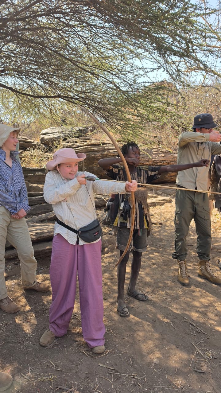 A young traveller learning to shoot a Hadzabe bow with a hunter's help