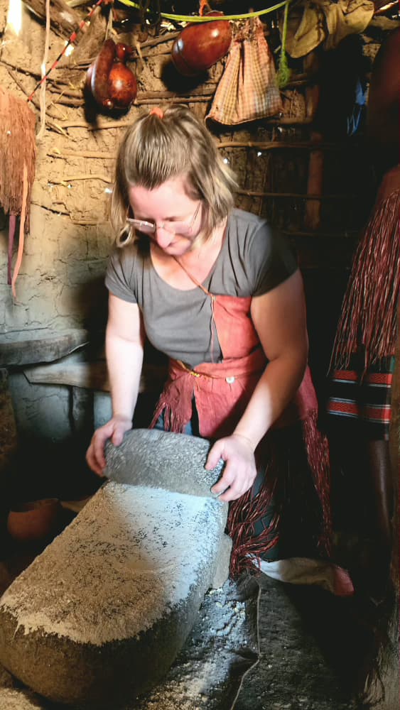 Traveller grinding maize on a stone quern inside a mud-walled hut