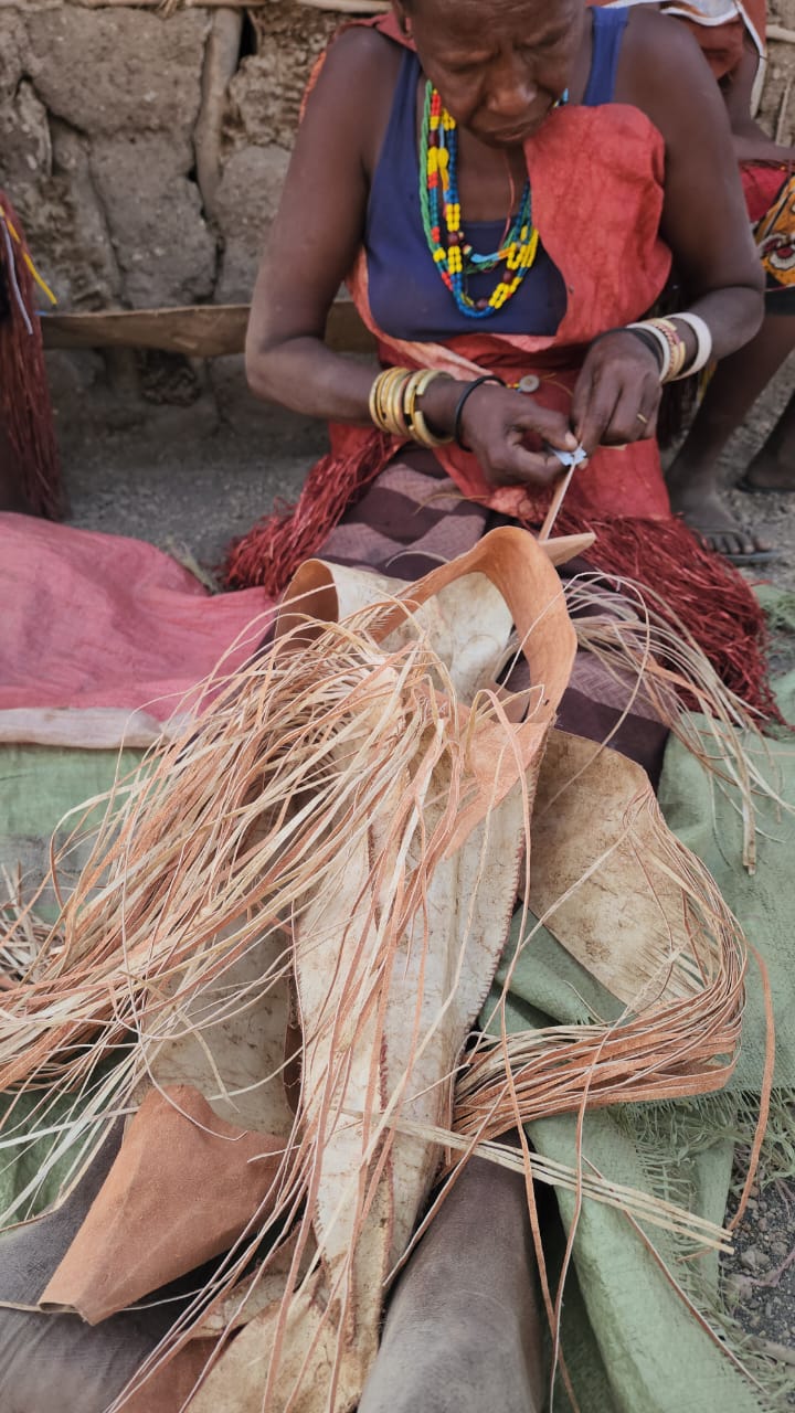 Datoga woman splitting palm fibres to weave in her homestead courtyard