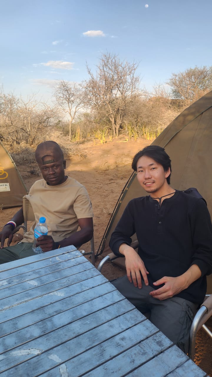 Guide and guest relaxing at the camp table beside the tents